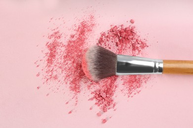 Makeup brush and scattered blush on pink background, top view