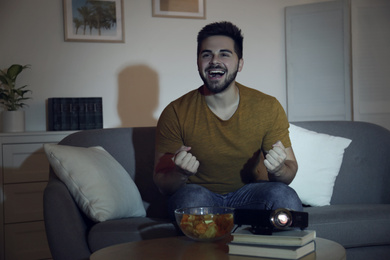 Photo of Happy young man watching movie using video projector at home