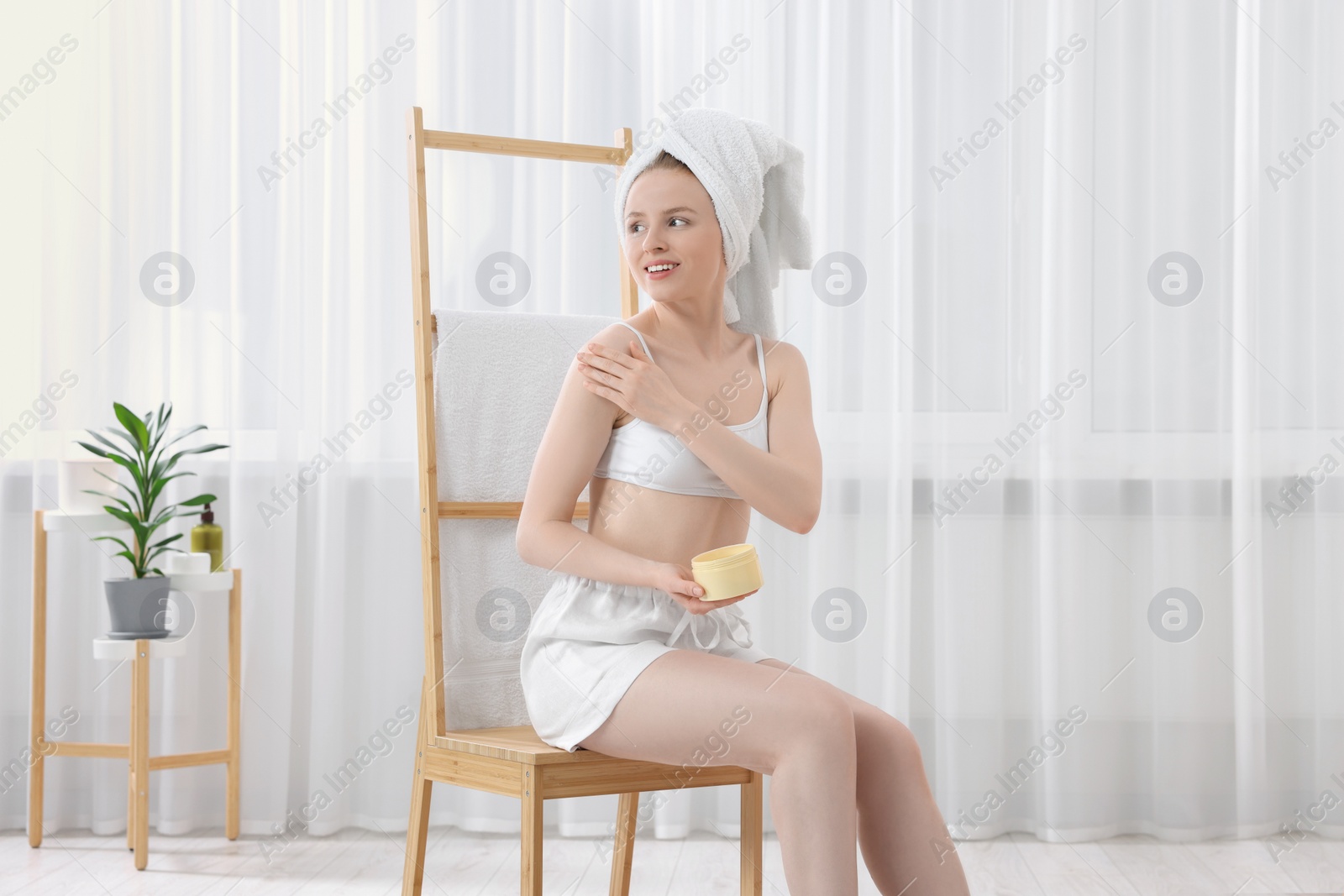 Photo of Beautiful young woman applying body cream onto shoulder indoors