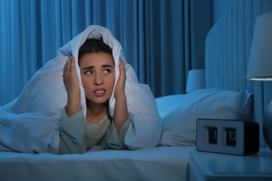 Photo of Unhappy young woman covering ears with blanket in bed at home. Noisy neighbours
