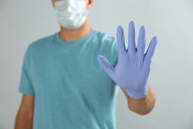 Man in protective face mask and medical gloves showing stop gesture on grey background, closeup