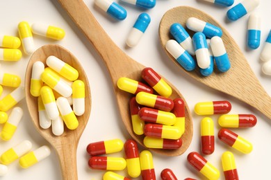 Antibiotic pills and spoons on white background, flat lay