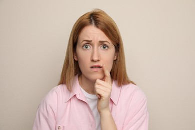 Photo of Upset woman with herpes applying cream on lips against beige background