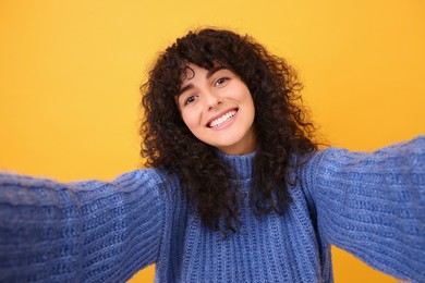 Photo of Beautiful young woman taking selfie on orange background