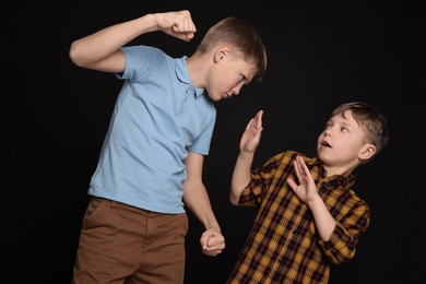 Photo of Boy with clenched fists bullying scared kid on black background