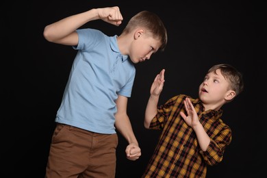 Boy with clenched fists bullying scared kid on black background