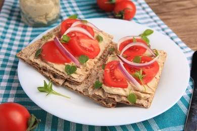 Photo of Fresh crunchy crispbreads with pate, tomatoes, red onion and greens on table