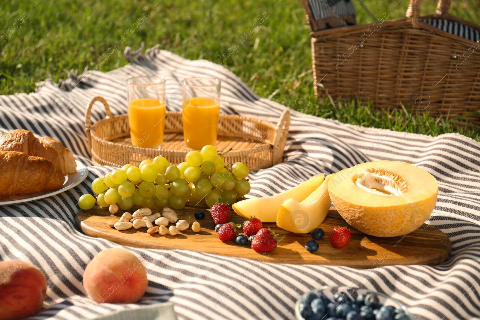 Photo of Picnic blanket with delicious food and juice on green grass outdoors