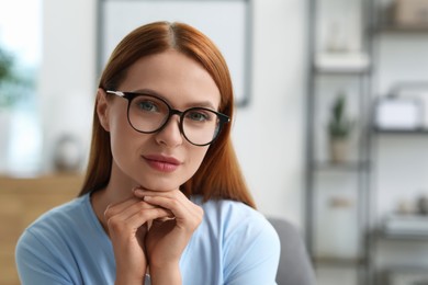 Photo of Portrait of beautiful young woman with red hair at home. Attractive lady in glasses looking into camera. Space for text