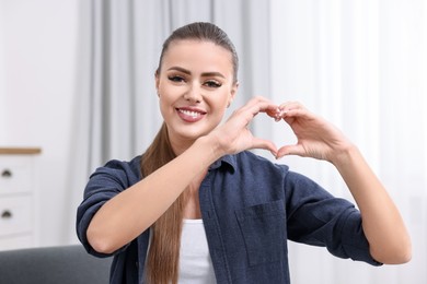 Photo of Happy woman showing heart gesture with hands at home