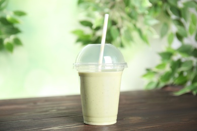 Photo of Tasty fresh milk shake in plastic cup on wooden table