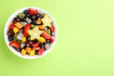 Photo of Delicious exotic fruit salad on green background, top view. Space for text