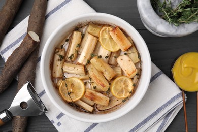 Dish with baked salsify roots, lemon, thyme and sauce on black wooden table, flat lay