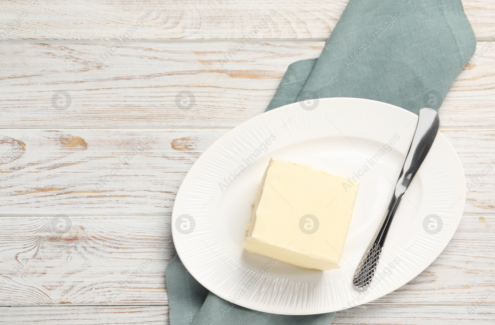 Photo of Block of tasty butter and knife on white wooden table. Space for text