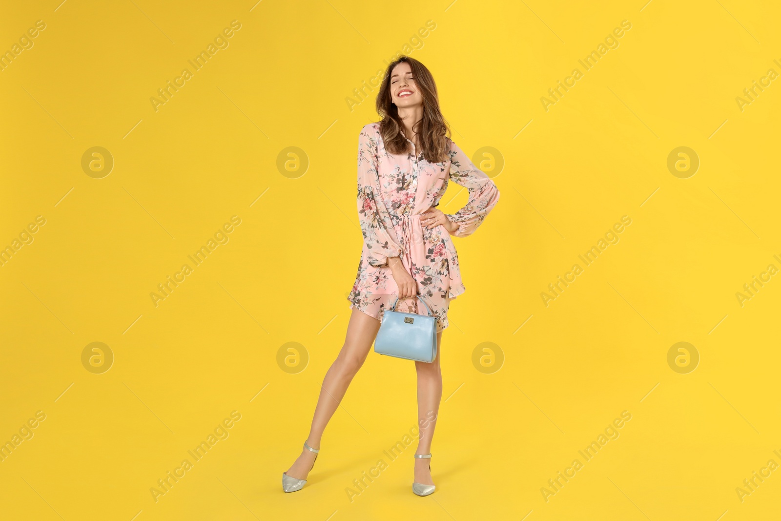 Photo of Young woman wearing floral print dress with stylish handbag on yellow background