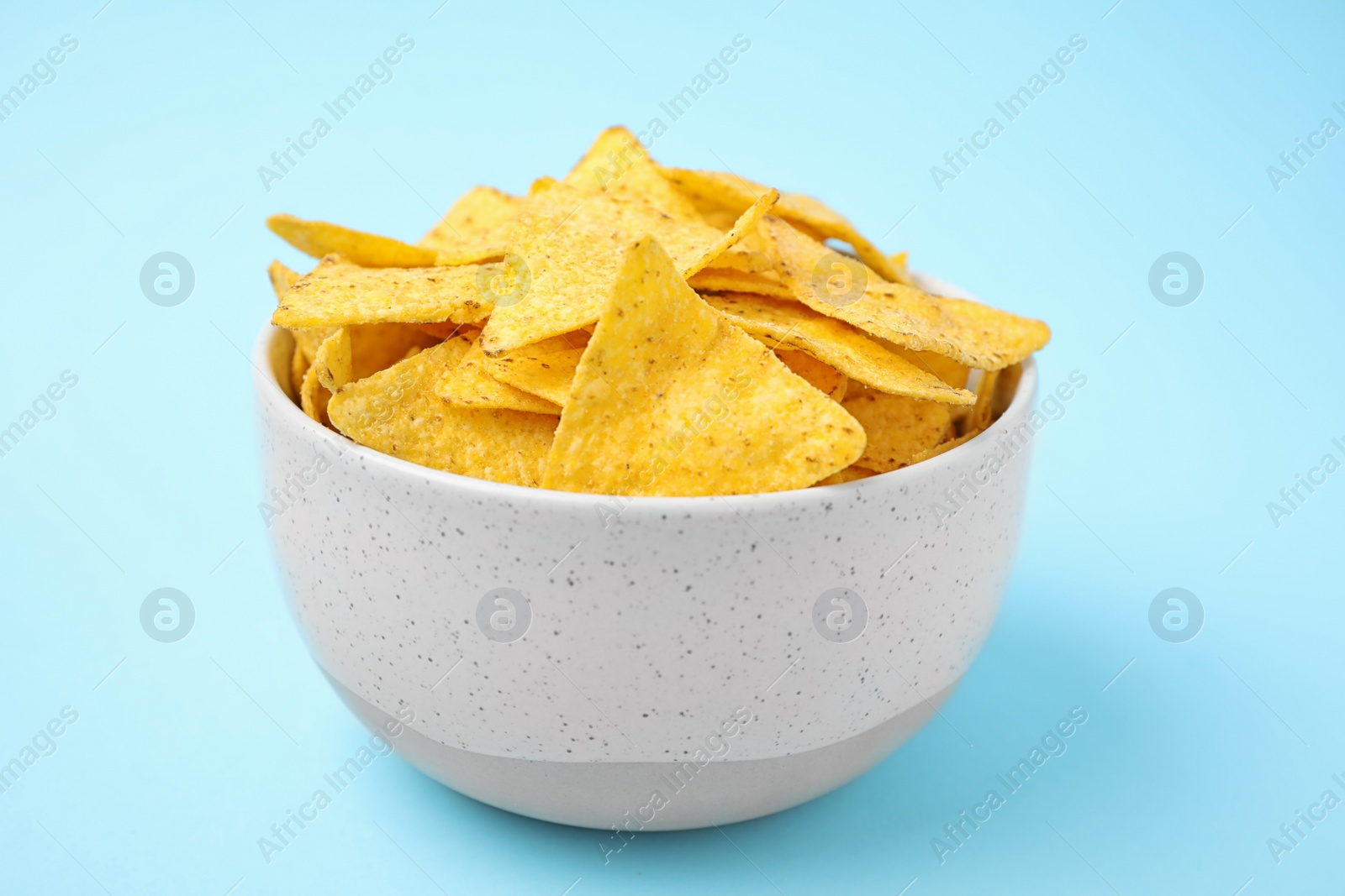 Photo of Bowl with tasty Mexican nachos chips on light blue background
