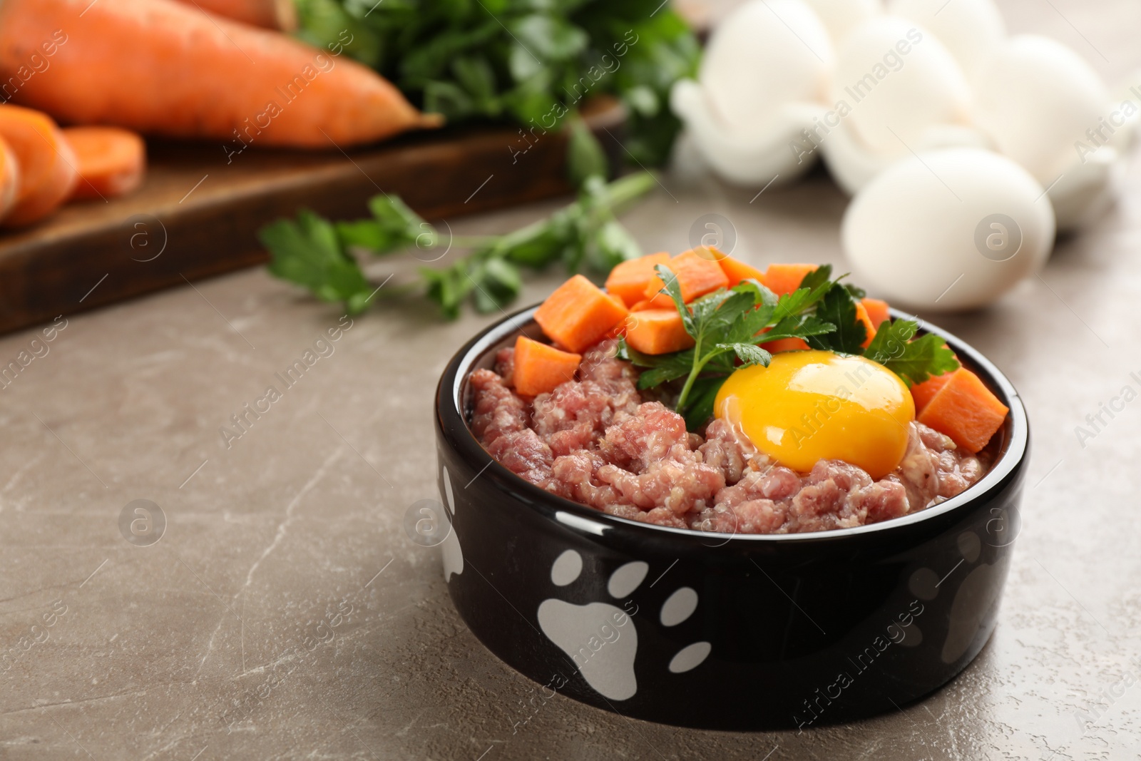 Photo of Natural pet food in feeding bowl on grey table, closeup. Space for text