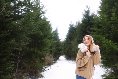 Young woman in snowy conifer forest, space for text. Winter vacation