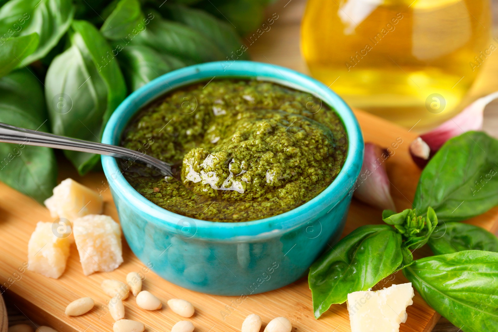 Photo of Tasty pesto sauce in bowl, basil, pine nuts, cheese and garlic on table, closeup