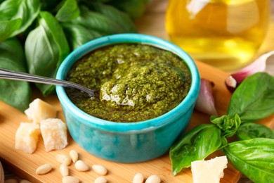 Photo of Tasty pesto sauce in bowl, basil, pine nuts, cheese and garlic on table, closeup