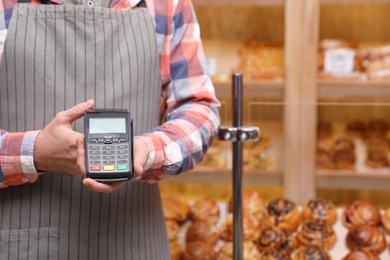 Cashier holding payment terminal in bakery, closeup. Space for text