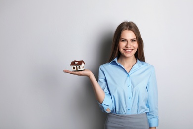 Photo of Beautiful real estate agent with house model on grey background