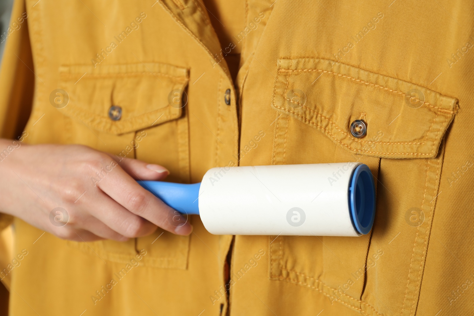 Photo of Woman cleaning yellow shirt with lint roller, closeup