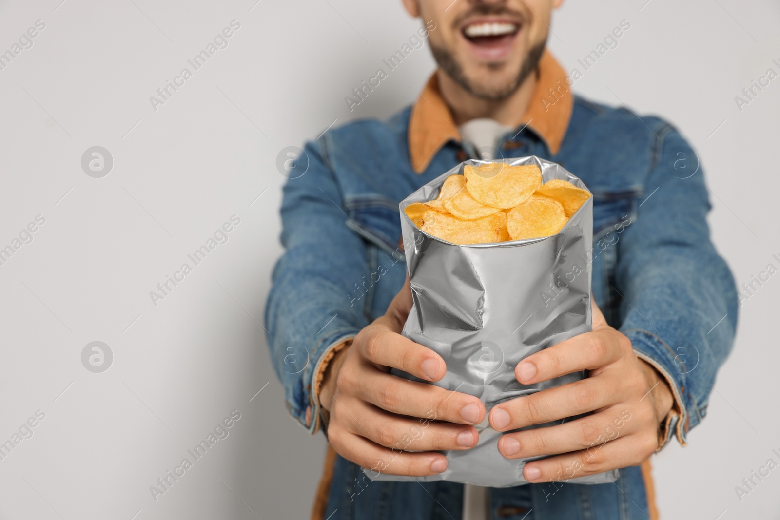 Photo of Handsome man with potato chips against light grey background, closeup. Space for text