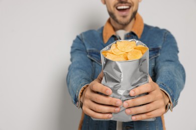 Photo of Handsome man with potato chips against light grey background, closeup. Space for text