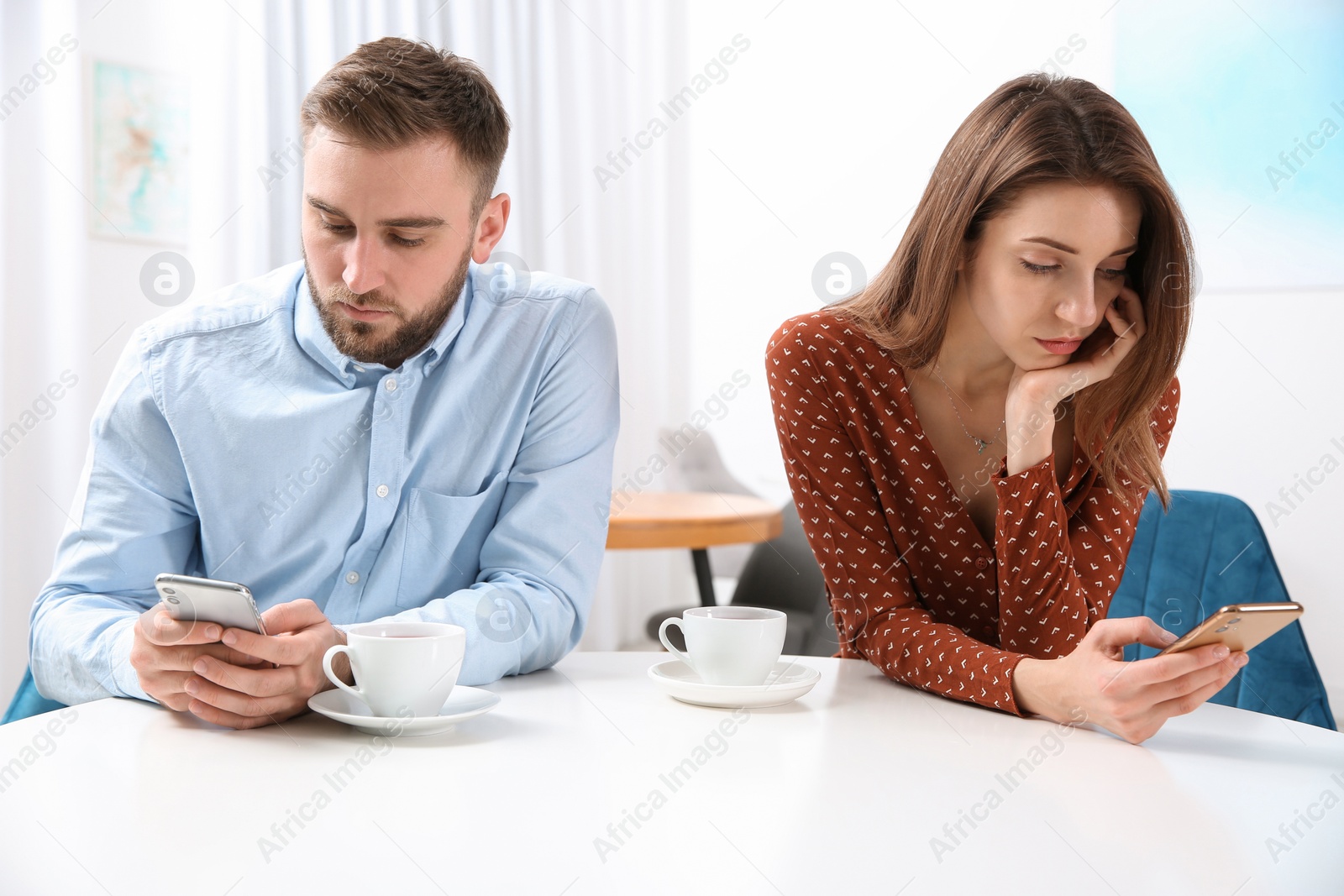 Photo of Couple addicted to smartphones ignoring each other in cafe. Relationship problems