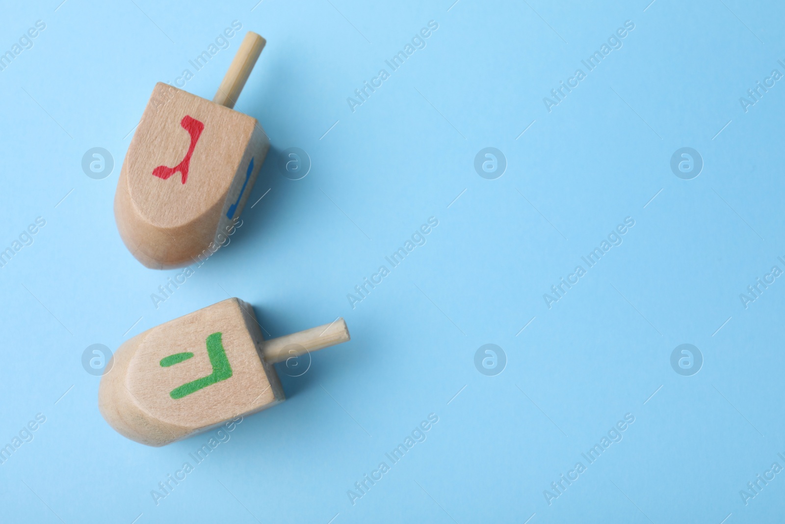 Photo of Hanukkah traditional dreidels with letters He and Gimel on light blue background, flat lay. Space for text