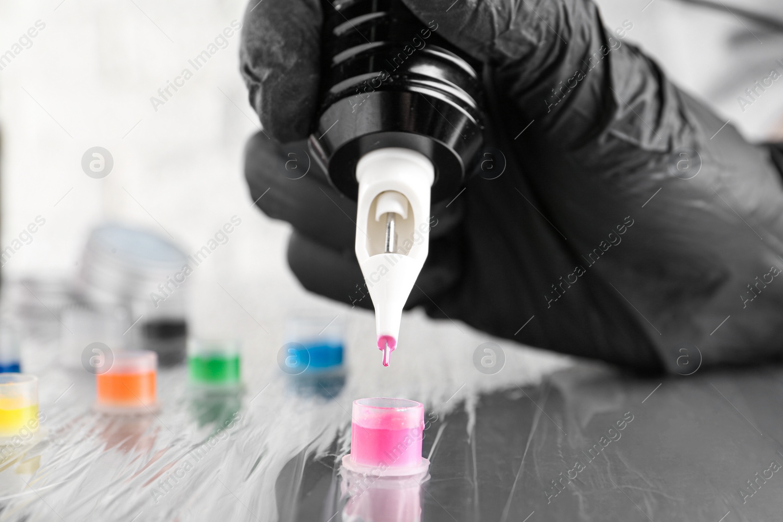 Photo of Tattoo artist with professional machine and colorful inks at table, closeup