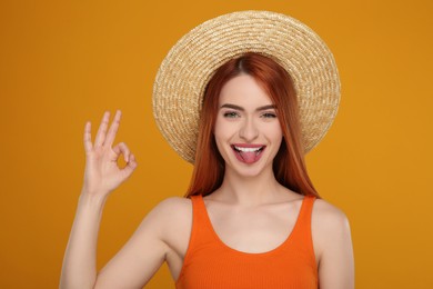 Happy woman showing her tongue and OK gesture on orange background