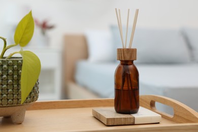 Photo of Aromatic reed air freshener near houseplant on wooden tray indoors