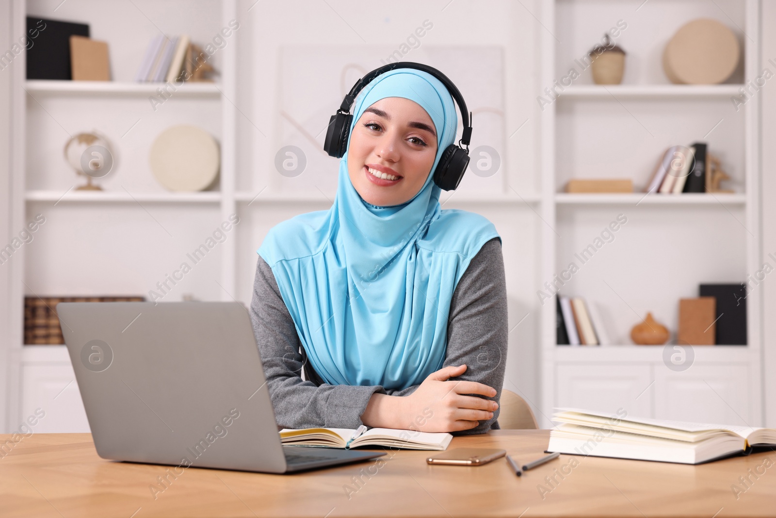 Photo of Muslim woman in hijab using laptop at wooden table in room