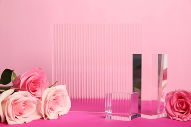 Photo of Stylish presentation of product. Beautiful roses and geometric glass figures on pink table