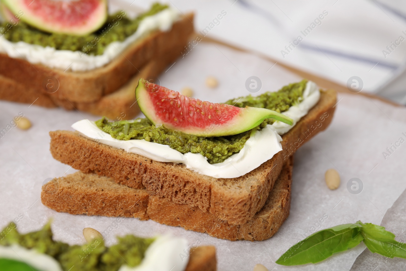 Photo of Tasty bruschetta with cream cheese, pesto sauce and fig on parchment paper