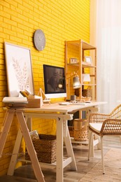 Stylish home office interior with comfortable workplace near yellow brick wall