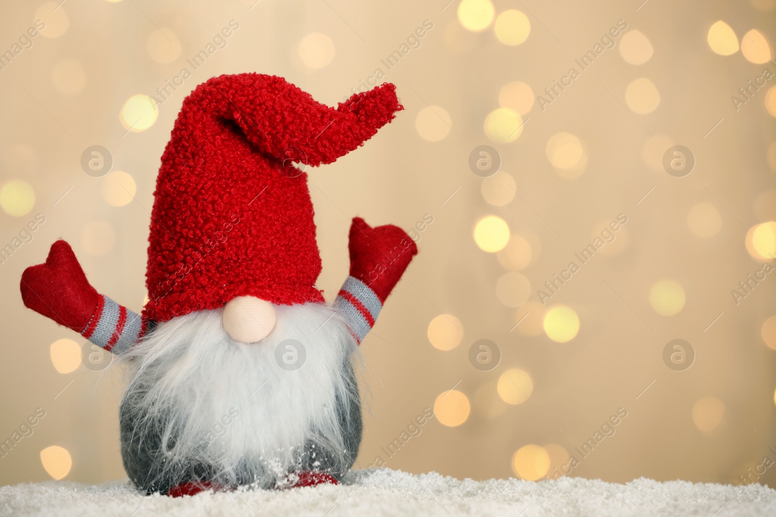 Photo of Cute Christmas gnome on snow against blurred festive lights. Space for text