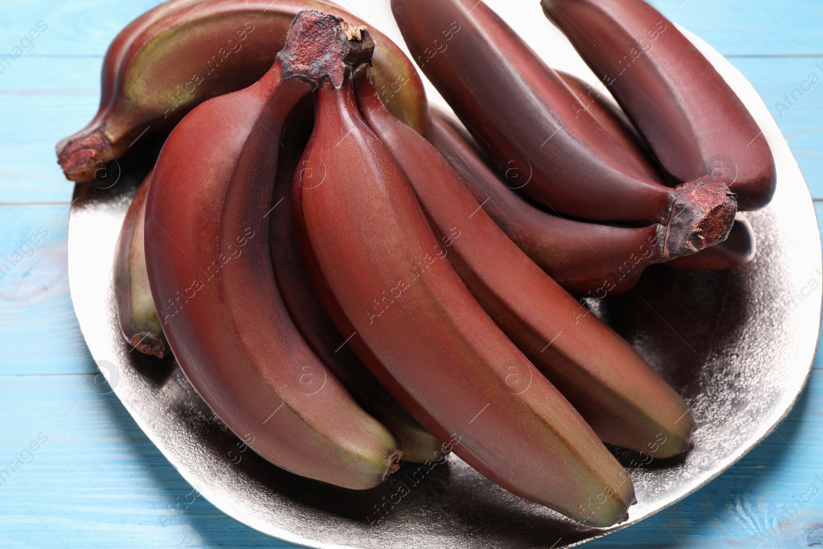 Photo of Tasty red baby bananas on light blue table, closeup