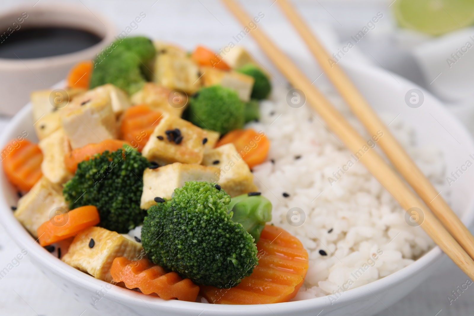 Photo of Bowl of rice with fried tofu, broccoli and carrots on table, closeup