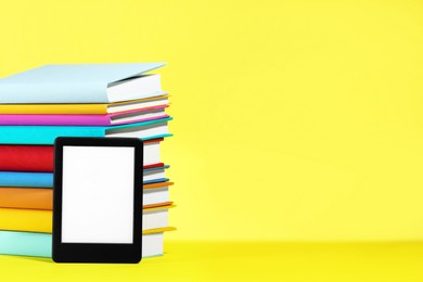 Photo of Modern e-book reader and stack of hard cover books on yellow background. Space for text