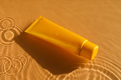 Photo of Tube with moisturizing cream in water on orange background