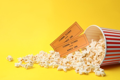 Photo of Bucket of fresh popcorn and tickets on yellow background, space for text. Cinema snack