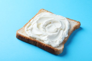 Photo of Slice of bread with tasty cream cheese on light blue background, closeup