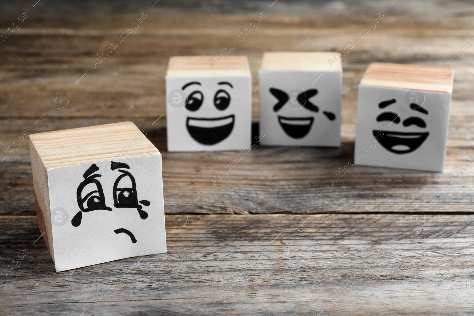 Photo of Cubes with sad and funny faces on wooden table. Bullying concept