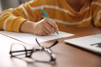 Woman writing letter at wooden table indoors, closeup