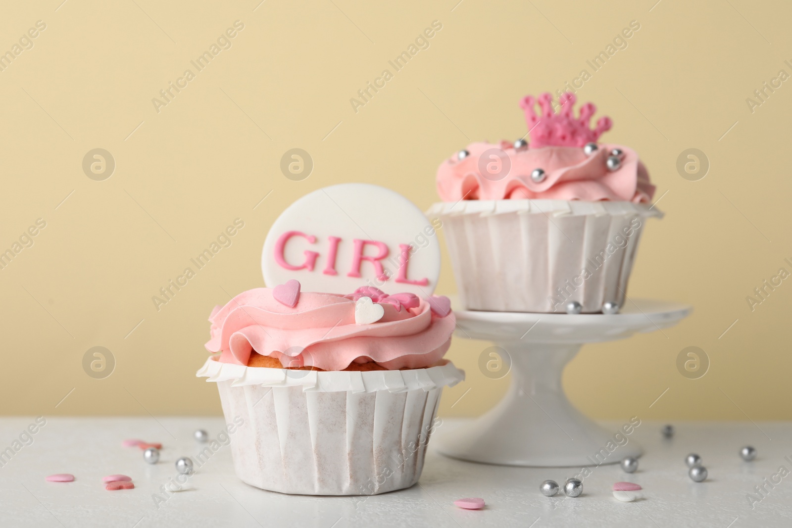 Photo of Delicious cupcakes with pink cream and toppers for baby shower on white table