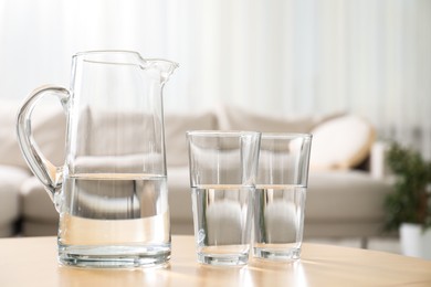 Photo of Jug and glasses with clear water on table indoors, closeup. Space for text
