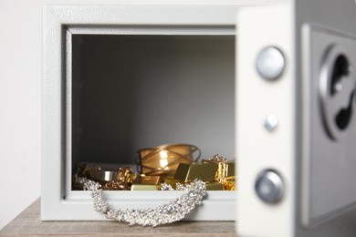 Photo of Open steel safe with gold bars and jewelry on wooden table against white background